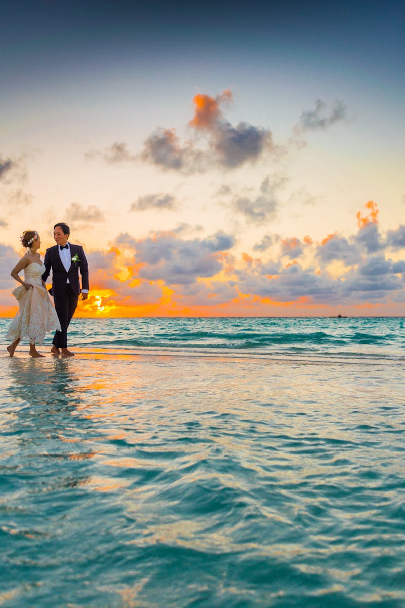A young couple enjoying a romantic beach wedding during a vibrant sunset.