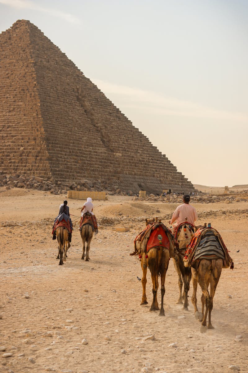 A group rides camels near an ancient pyramid in Egypt's Sahara Desert.