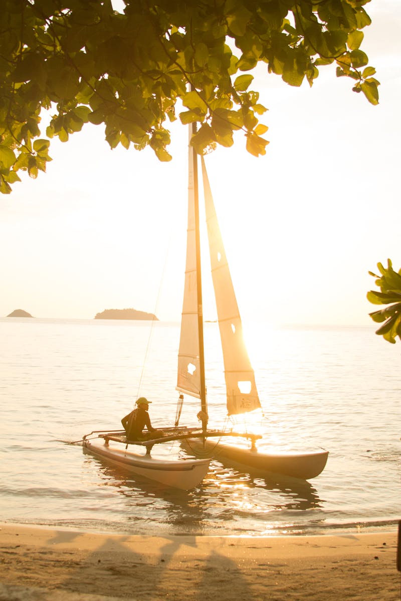 A sailboat glides at sunset on a tranquil tropical beach in Thailand.
